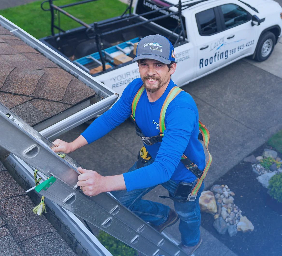 Lacey Roofing crew member climbing a ladder next to a home roof, smiling at camera